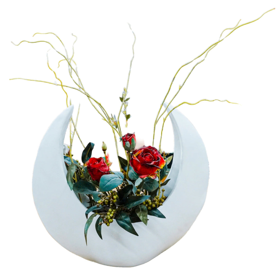 Decorative planter shaped like a crescent moon with red flowers and greenery on a white background