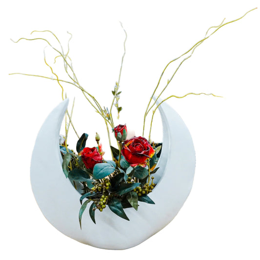 Decorative planter shaped like a crescent moon with red flowers and greenery on a white background