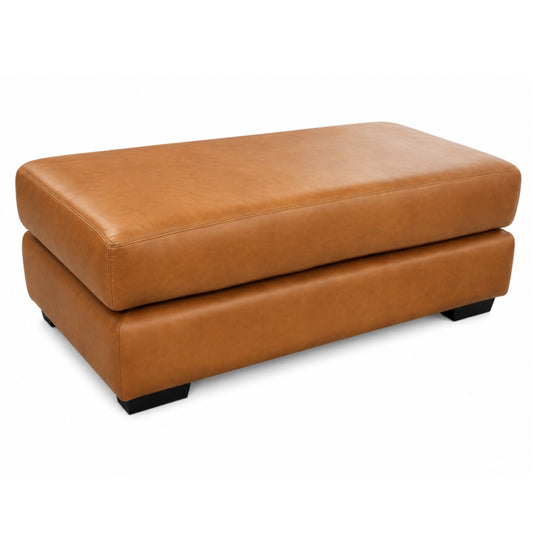 A rectangular tan leather ottoman with a raised seat cushion and short black feet, photographed on a clean white background.